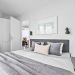 Schlafzimmer mit Bett, Wandbild und Nachttisch. Tür führt in Wohnbereich.