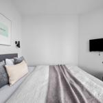 Schlafzimmer mit Bett, Wandbild und TV. Wandlampe und graue Polster.