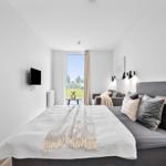 Schlafzimmer mit Bett, Fernseher und Fensterblick auf Grünfläche.