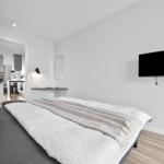 Schlafzimmer mit Bett, Wand-TV und Blick in die Küche.