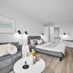 Zimmer mit Sofa, Bett, TV und Wandbild. Holzboden und moderne Einrichtung.