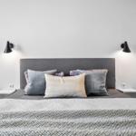Schlafzimmer mit Bett, Kissen und Wandlampen. Links ist ein Sofa sichtbar.