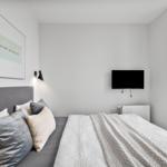 Schlafzimmer mit Bett, Wandbild und Fernseher. Große Fensterfront mit Blick.