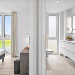 Schlafzimmer mit Blick auf Grünfläche. Nebenraum mit Badewanne, Waschbecken und Toilette.