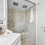 Moderne Dusche mit Glaswand, Duschbrause und Handtuch. Waschbecken mit Seife und Spiegel.