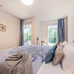 Schlafzimmer mit Doppelbett, Fenstern und Wandbildern.