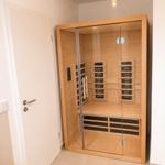 Innenraum einer Sauna mit Holzwand und Glasfront. Deckenlampe und Tür sind sichtbar.