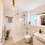 Badezimmer mit Dusche, Waschbecken und Toilette. Holzdekoration und Pflanzen.