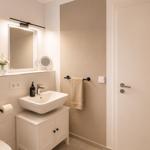 Badezimmer mit Waschbecken, Spiegel und Handtuchhalter. Fenster und Toilette sind sichtbar.