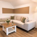 Wohnzimmer mit Ecksofa, Tisch und Stehlampe.