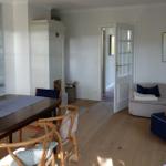 Essbereich mit Tisch und Stühlen, Wohnbereich mit Sofa und Kissen, Holzboden und Wandbild.