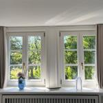 Zwei Fenster mit grauen Vorhängen und Blumen auf dem Fensterbrett.