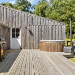 Holzterrasse mit Whirlpool, Grill und rustikalem Haus. Grün hinter dem Gebäude.