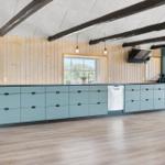 Küche mit hellblauen Schränken, Holzwänden und schwarzen Balken an der Decke.