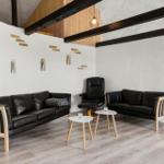 Zwei schwarze Sofas, ein Sessel und zwei Tische in einem Raum mit Holzbalken und Fenster.