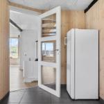 Küche mit weißem Kühlschrank und Holzwänden. Tür führt in Wohnbereich mit Fenster.