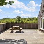 Holzterrasse mit Picknicktisch, Blick auf Wald und Himmel.