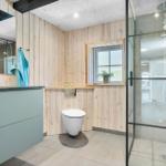 Badezimmer mit Dusche, Toilette und Waschbecken. Holzwände und Fenster.