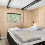 Schlafzimmer mit Holzwänden, Bett und Fenster mit Blick auf Bäume.