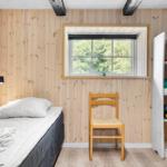 Ein Schlafzimmer mit Holzwand, Bett, Stuhl und Bücherregal. Fenster zeigt Wald.