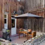 Terrasse mit Tisch, Stühlen und Sonnenschirm vor Holzhauswand