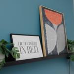 Schwarze Ablage mit Bildern und Pflanzen an blauer Wand