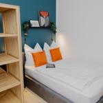 Schlafzimmer mit Bett, orangefarbenen Kissen und Holzregal an der Wand.