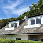 House with dormer windows and balcony, surrounded by trees under blue sky.