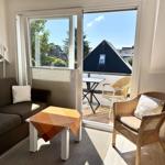 Living room with sofa, armchair, and balcony with table and chairs.