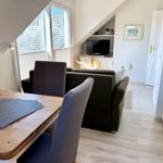 Dining area with table and chairs, living area with sofa and TV, kitchen with white cabinets.