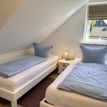 Two single beds with blue pillows and bedding. Window with view of roof tiles.