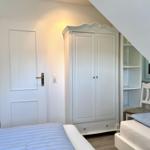 Room with two beds, wardrobe, and chair under sloped ceiling.