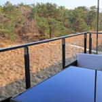 Terrace with table and chairs, view of forest and grassy area.
