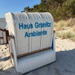 White beach chair with inscription Haus Granitz Ambiente stands on sand before trees.