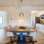 Dining area with table, chairs, and modern lighting. Kitchen with counter and refrigerator.