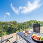 Terrasse mit Tisch, Stühlen und Obst. Blick auf Wald und Meer.