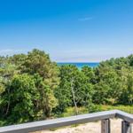 Blick von Balkon auf Wald und Meer unter blauem Himmel