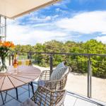 Terrasse mit Tisch, Stühlen und Blick auf Wald und Strand.