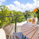 Terrasse mit Tisch, Stühlen und Blick auf grüne Bäume unter blauem Himmel.