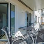 Terrasse mit Tisch und Stühlen, Glas-Türen zum Innenraum, Blick auf benachbarte Gebäude.