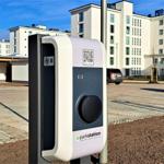 E-Ladesäule im Außenbereich vor Wohnhäusern mit Parkplatz und gepflastertem Boden.