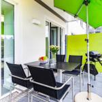 Terrasse mit Tisch, Stühlen, Grill und grünem Sonnenschirm. Blick auf grüne Landschaft.