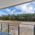 Terrace with glass railing offers view of sandy beach and forest.