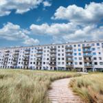 Apartment building with balconies and path through grassland under blue sky.