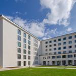 Modern multi-family building with white facade and green lawn area under blue sky.