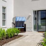 House with terrace, blue-and-white beach chair, and shrub beds.