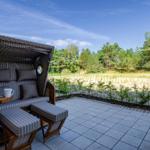 Terrace with beach chair, laptop, and cup. View of meadow and forest.