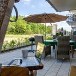 Terrace with table, chairs, and umbrella. Laptop and cup on a table.