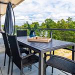 Terrasse mit Tisch, Stühlen und Sonnenschirm. Blick auf grüne Bäume und Himmel.
