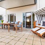 Terrasse mit Holztisch, Stühlen und Strandkorb mit Streifenbezug.